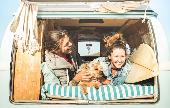 Hipster couple with cute dog traveling together on vintage mini van transport - Life inspiration concept with hippie people on minivan adventure trip in relax moment - Bright warm retro filter