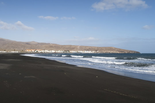 dark sand beach near Tarajalejo on Fuerteventura island against blue sky