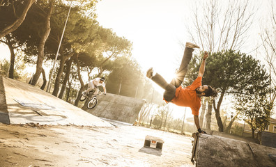 Urban athlete breakdancer performing acrobatic jump flip at skate park - Guy riding bmx bicycle behind mate acrobat dancing with extreme move - Breakdance and friendship concept - Warm sunset filter