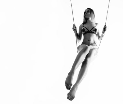 Perfect slim girl with a rope posing on a light background. Woman with sexy athletic body on a swing. free space for your text. black and white
