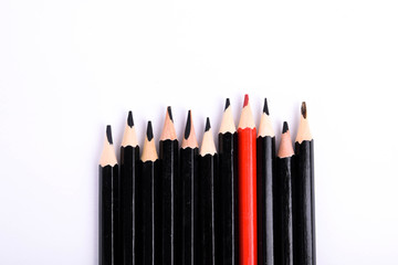 Red pencil standing out from crowd of plenty identical black fellows on white table. Leadership,...