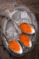 Delicious bright red fresh snack red caviar on a wooden background. Silver spoon with caviar. Expensive luxury delicacy seafood.
