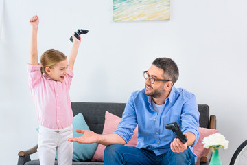kid celebrating success while playing video game together with father at home