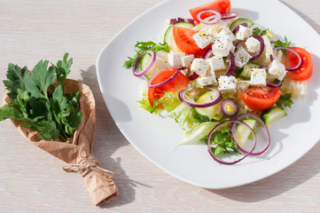 Fresh spring salad with cucumber, tomato, cheese and arugula isolated on a white plate Bouquet of fresh green parsley leaves in white  craft paper