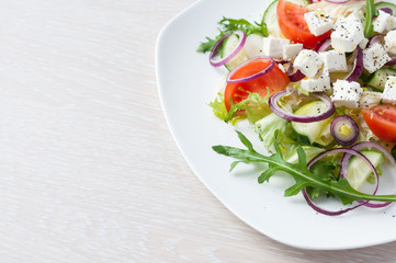 Fresh spring salad with cucumber, tomato, cheese and arugula isolated on a white plate 