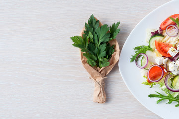 Fresh spring salad with cucumber, tomato, cheese and arugula isolated on a white plate Bouquet of fresh green parsley leaves in white  craft paper