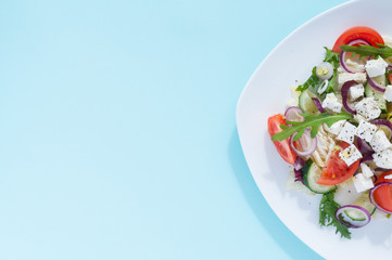Fresh spring salad with cucumber, tomato, cheese and arugula isolated on a white plate 