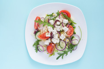 Fresh spring salad with cucumber, tomato, cheese and arugula isolated on a white plate 