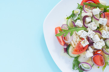Fresh spring salad with cucumber, tomato, cheese and arugula isolated on a white plate 