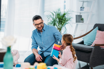 little daughter and father playing with colorful blocks together on floor at home