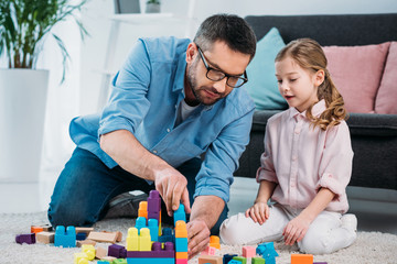 little daughter and father playing with colorful blocks together on floor at home