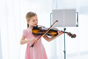 smiling little child in pink dress playing violin at home © LIGHTFIELD STUDIOS