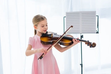 smiling little child in pink dress playing violin at home