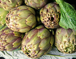 Fresh purple and green artichokes with green leaves on black background, close up 