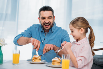 cheerful father and little daughter having breakfast at home