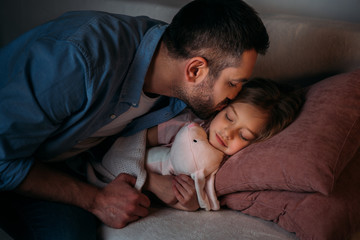 father kissing cute sleeping daughter with toy in hands