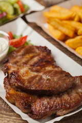 Grilled pork neck served on paper trays.