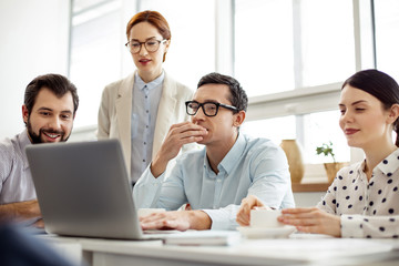 Working team. Handsome concentrated dark-haired man wearing glasses and working on his laptop and his colleagues sitting near him