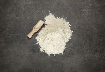 Handful sifted pastry flour and scoop with flour on grey surface