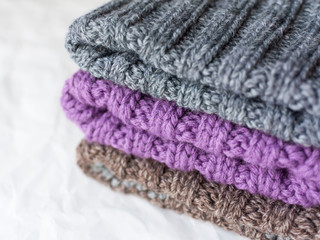 Fototapeta na wymiar A pile of handmade knitted hats of gray, lilac and brown colors on white bokeh background close up