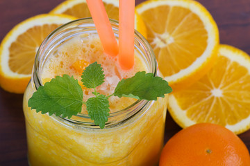 Smoothies from orange and tangerine with mint on wooden background