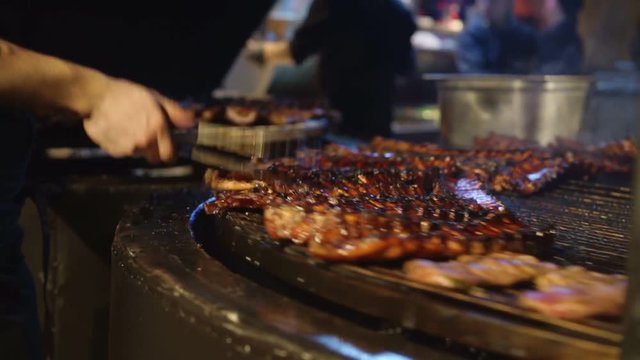 Chef cooking ribs on grill. Male hand holding kitchen stainless steel tongs, appetizing pork ribs on cast iron grill. Restaurant kitchen, cookin
