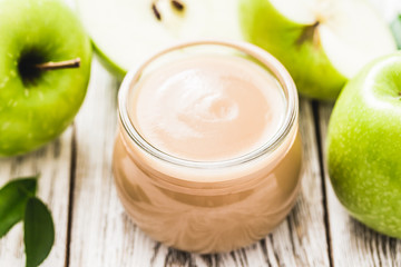 Vegan applesauce in glass jar and green apples on rustic white wooden background. Selective focus, space for text.
