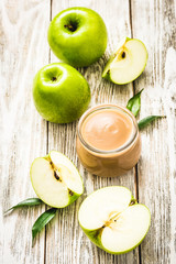 Baked applesauce in glass jar and green apples on shabby white wooden background. Selective focus, space for text. 
