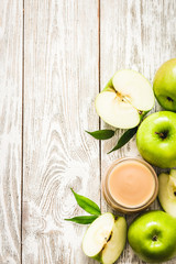 Homemade applesauce in glass jar and green apples on shabby white wooden background. Top view, copy space.