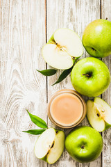 Applesauce in glass jar and green apples on shabby white wooden background. Top view, copy space.