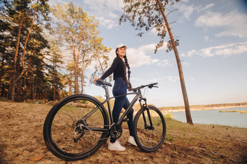 Fototapeta na wymiar A beautiful racer stands on the edge of a lake with a bicycle. Spring, healthy lifestyle, ecology, advertising HLS, place for text, social networks.