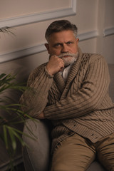 serious senior man sitting in armchair and looking at camera