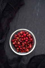 pink pepper in small bowl on black ceramic background