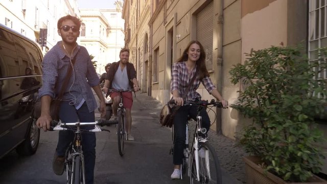 Three young friends tourists riding bikes in small street in Rome city centre on sunny day slow motion camera car steadycam