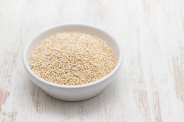 uncooked quinoa in white bowl on white wooden background