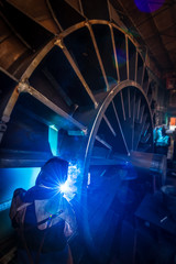 Man with special protection equipment welding big iron wheel. Warning - authentic shooting in...