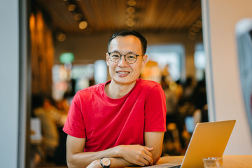 A portrait of cheerful Asian Chinese guy dressed comfortably in a casual red shirt and khaki pants....