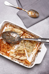 Fototapeta premium Dish of leftover pasta bake and cheesy garlic bread with a spoon and napkin on a grey rustic background