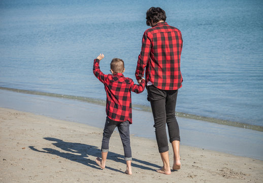 Father and son walking along beach, holding hands, rear view
