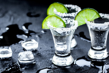 Silver tequila shots with ice and lime on black table background