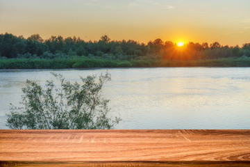 Empty wooden table with summer background of riverside at sunset. Can be used for display or montage products