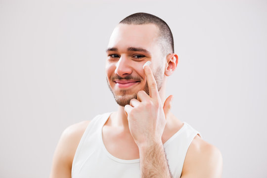 Young man who is applying skin cream on his face. 
