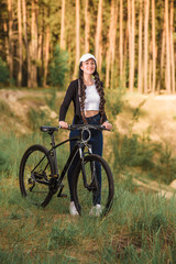 Casual and sport. Adorable girl with long straight fair hair wearing streetwear is posing on the bicycle on the natural forest background