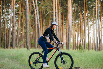 Great beginning of the day. Cute girl is on a bike outdoors in nice spring park, wearing jacket and trendy sports outfit, sneakers, smiling. pring, ecology, advertising HLS, social networks.