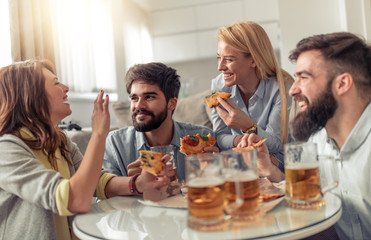 Happy friends eating pizza and watching tv at home