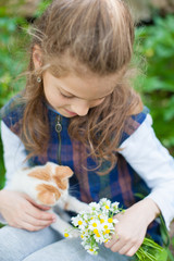 happy little girl holding bouquet of flowers playing with little cat on her hands