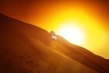 Fototapeta na wymiar Offroad truck or suv riding dune in arabian desert at sunset. Offroad has been modified to be unrecognized.