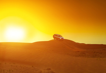Fototapeta na wymiar Offroad truck or suv riding dune in arabian desert at sunset. Offroad has been modified to be unrecognized.