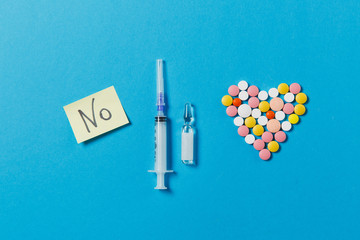 Medication white, colorful round tablets in form of heart isolated on blue background. Pills ampoule, paper sticker sheet text No, empty syringe needle. Concept of treatment, choice healthy lifestyle.