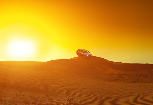 Offroad truck or suv riding dune in arabian desert at sunset. Offroad has been modified to be unrecognized.